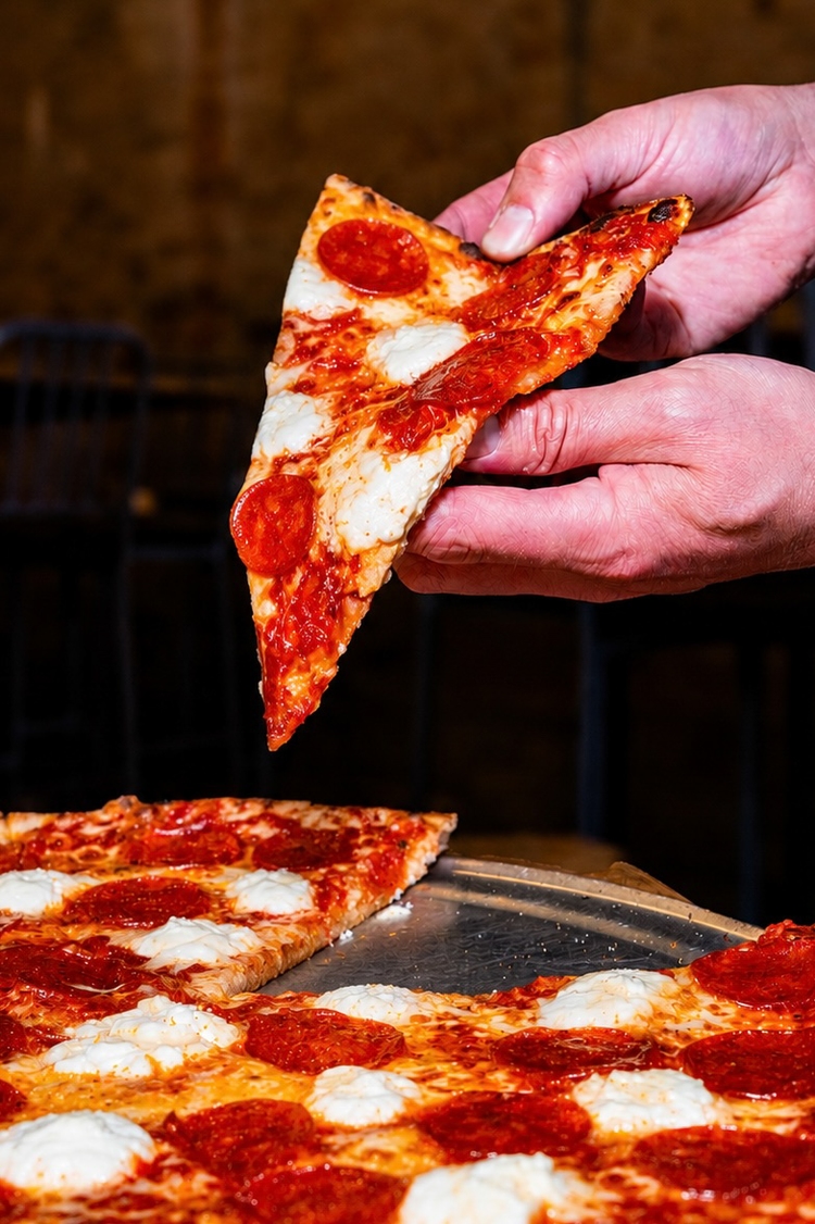 A folded New York-style pepperoni slice, held in one hand.