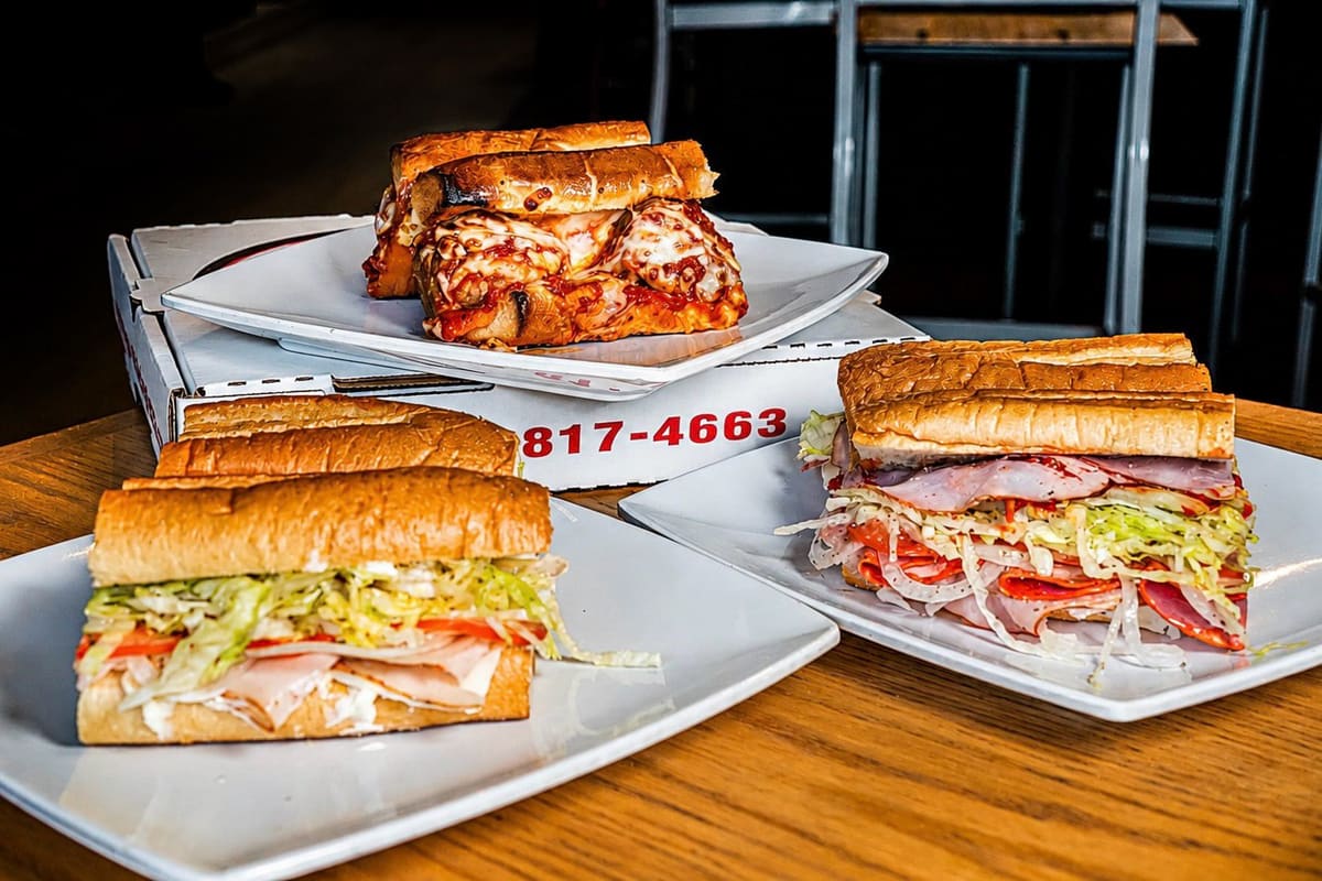 Good Side subs and a pie on the table, pizza boxes stacked behind.