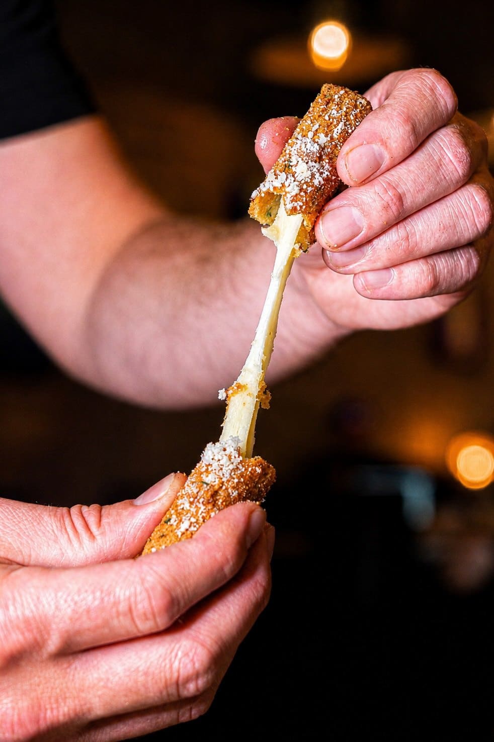 A fried cheese stick pulled apart, cheese stretching