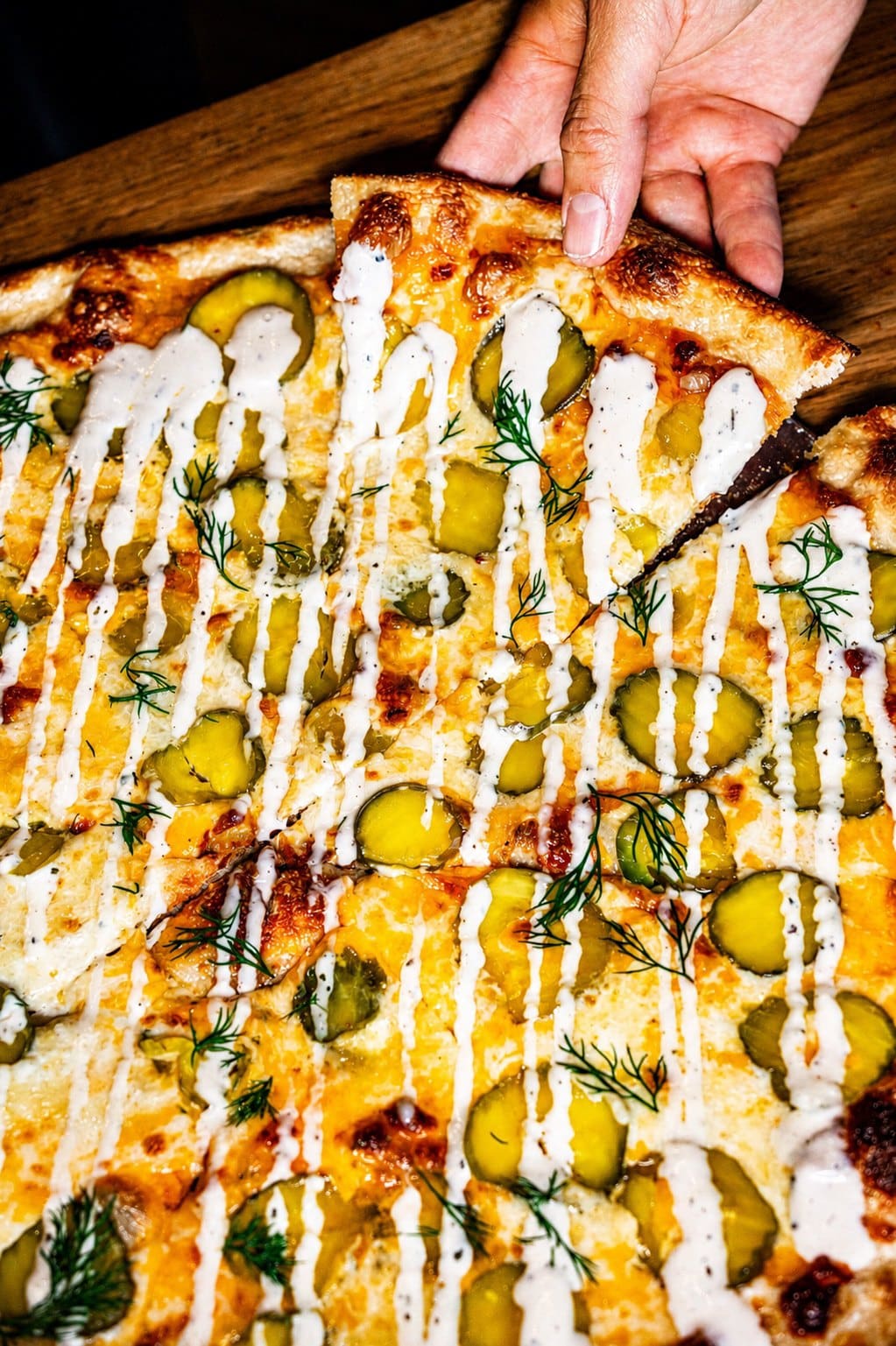 A hand pulling a slice of pickle pizza